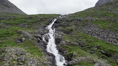 Aerial-dolly-shot,-pulling-out-from-a-narrow,-rushing-river-as-it-winds-down-a-steep,-rocky,-mossy-hillside,-Trollstigen,-Norway