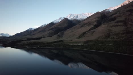 Aerial-flying-towards-perfectly-reflected-snow-capped-mountains-at-sunset-near-Queenstown-New-Zealand