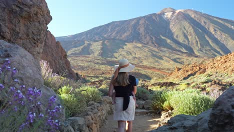 Young-blonde-mother-carrying-child-and-walking-in-majestic-Tenerife-landscape