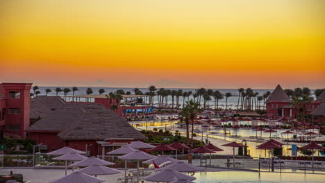 Wunderschöne-Zeitrafferaufnahmen-Des-Sonnenuntergangs-In-Einem-Großen-Hotel-Am-Strand-Mit-Pool,-Sonnenschirmen,-Palmen-Und-Natur