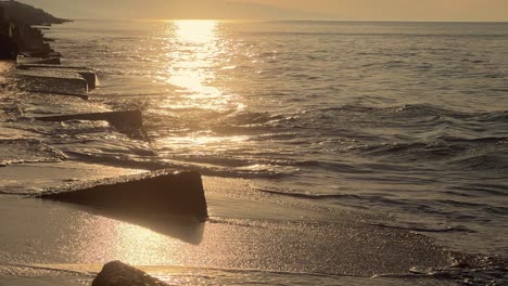 Cubes-and-blocks-of-concrete-scatter-along-the-shoreline,-gently-touched-by-waves,-partially-immersed-in-sand,-embracing-the-coastal-defense-theme-with-a-conceptual-touch