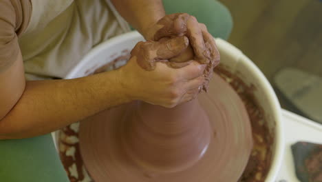 Skilled-craftsman-forming-wet-clay-vessel-spinning-on-pottery-wheel