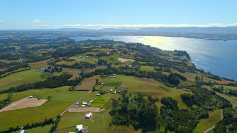 Paisaje-Panorámico-De-Drones-Aéreos-De-La-Isla-Lemuy-En-Chiloé-Patagonia-Chilena-Cielo-Y-Reflejo-Del-Sol-Sobre-El-Agua-Del-Mar-Y-La-Tierra-De-Los-Islotes-Verdes