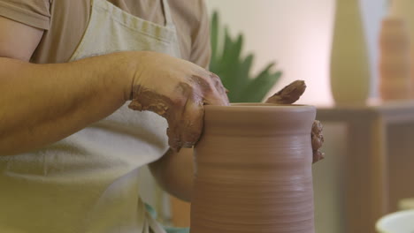 Pottery-artist-working-raw-clay-vase-edge-on-workshop-turntable-wheel-applying-pressure