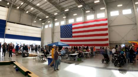 Large-hangar-with-American-flag-hanging,-civilians-filling-the-space-for-a-civilian-tour-of-the-naval-air-station