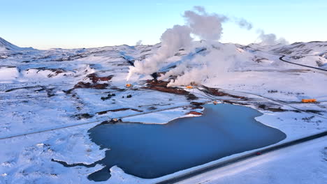 Paisaje-Geotérmico-Cubierto-De-Nieve-Con-Respiraderos-De-Vapor,-Camino-Junto-Al-Lago-En-Myvatn-Durante-El-Invierno,-Vista-Aérea