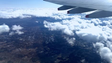 Aerial-view-from-airplane-window-overlooking-clouds-and-landscape,-daylight