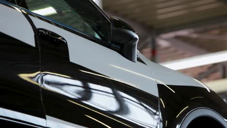 Close-up-of-a-sleek-black-car-in-a-well-lit-garage,-highlighting-the-modern-design-and-shiny-finish