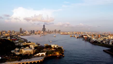 Golden-hour-view-of-a-bustling-city-harbor-with-ships-and-skyline,-aerial-perspective