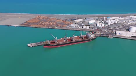 A-cargo-ship-docked-at-timaru-port,-new-zealand,-vibrant-turquoise-water,-aerial-view