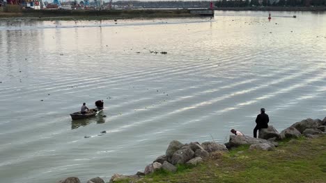 fisherman-row-paddle-scull-an-old-wooden-traditional-fishing-boat-using-plastic-net-to-catch-fish-in-harbor-alone-fisherman-try-to-expand-circle-net-stand-on-seaside-beach-anzali-bay-urban-life-iran