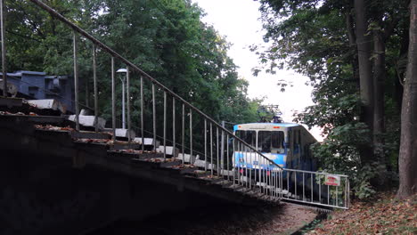 Funicular-Blanco-Y-Azul-Bajando-Por-Un-Ferrocarril-De-Pendiente-Pronunciada-En-Un-Parque-Verde-En-La-Ciudad-De-Kiev,-Ucrania,-Transporte-Público,-Toma-Estática-De-4k