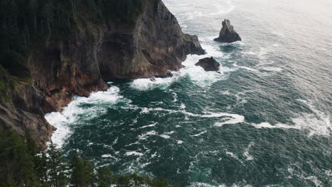 Flyover-above-evergreen-trees-on-rocky-cliff-above-Pacific-Ocean,-Oregon-Coast