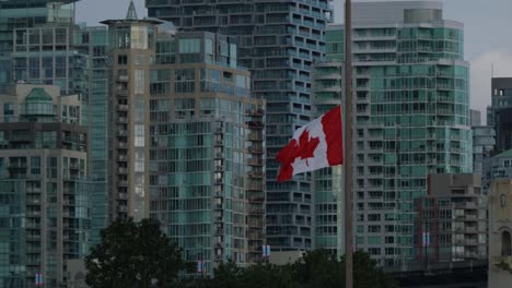 Ondeando-La-Bandera-Canadiense-En-Cámara-Lenta-Con-Los-Edificios-De-La-Ciudad-De-Vancouver-Al-Fondo,-La-Ciudad-De-Vancouver,-Columbia-Británica,-Canadá