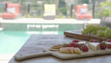 vegetarian-cheese-and-fruit-appetiser-served-on-luxury-resort-spa-hotel-with-swimming-pool-in-background