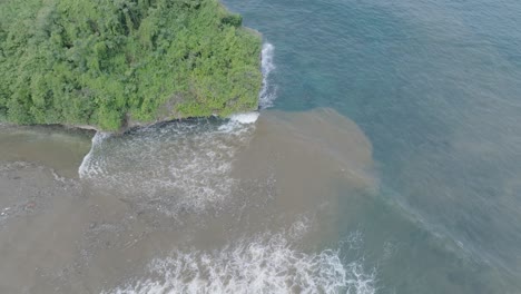 Top-down-aerial-drone-shot-over-polluted-sewage-water-and-floating-trash-with-debris-over-dead-coral-reef-mixing-with-turquoise-water-and-tropical-coastine-in-Bali-Indonesia