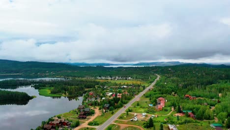 Panoramablick-Auf-Eine-Wunderschöne-Bergstadt-In-Einem-Wald-Mit-Atemberaubenden-Wolkigen-Hügeln-Im-Hintergrund-Eines-Ruhigen,-Klaren-Sees-Und-Der-Spiegelung-Der-Wolken-Auf-Dem-Wasser