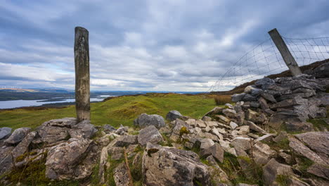 Panorama-Zeitraffer-Der-Ländlichen-Landschaft-Mit-Steinmauern,-Holzpfeilern-Und-Schafen-Auf-Einer-Wiese-Sowie-Hügeln-Und-Einem-See-In-Der-Ferne-An-Einem-Bewölkten-Tag,-Gesehen-Von-Carrowkeel-In-Der-Grafschaft-Sligo-In-Irland