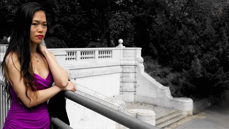 Woman-in-pink-dress-leaning-on-a-white-balustrade-in-City-Park-in-Vienna,-Austria,-trees-in-background,-selective-color