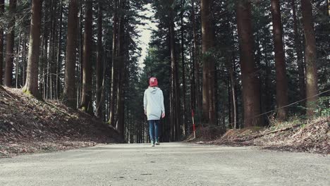 woman-walks-away-from-the-camera-in-the-middle-of-the-road-surrounded-with-trees
