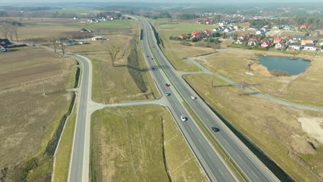 Aerial-view-of-cars-on-a-highway-near-a-rural-residential-area-with-fields