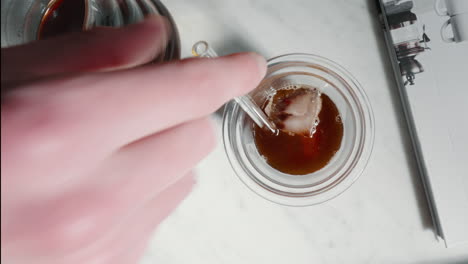 Hand-stirring-iced-coffee-in-transparent-glass-on-marble-surface