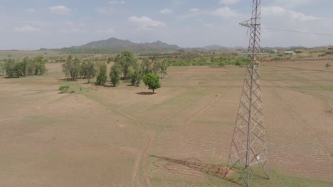 Aerial---Rising-drone-shot-by-power-tower-revealing-vast-field-with-mountain