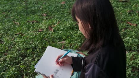 Overhead-static-shot-of-young-female-student-drawing-on-her-sketchbook-in-an-outdoor-park-setting