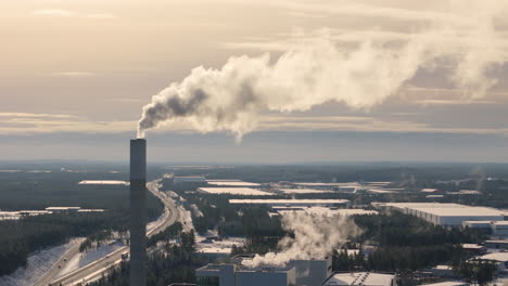 Smokestack-emitting-greenhouse-gases-against-golden-hour-sky,-telephoto-aerial