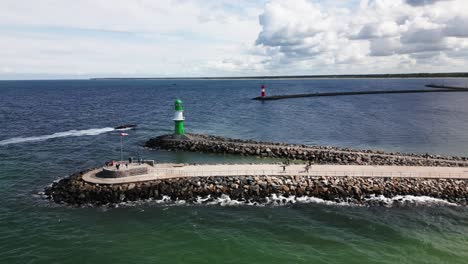 motorboat-enters-the-harbor,-two-pier-lights-at-the-harbor,-lighthouse,-baltic-sea,-warnemünde,-drone