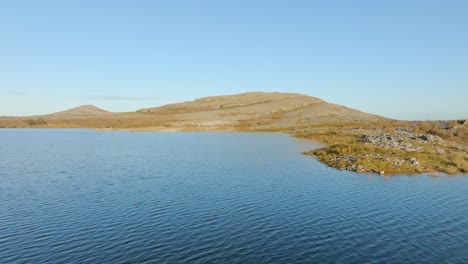 Aerial-pullback-over-textured-water-and-grassy-hills-of-sharp-limestone,-the-Burren-Ireland