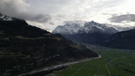 Atemberaubende-Schweizer-Berge-Mit-Epischen-Lichtstrahlen,-Die-Zwischen-Den-Wolken-über-Den-Feldern-Hindurchziehen