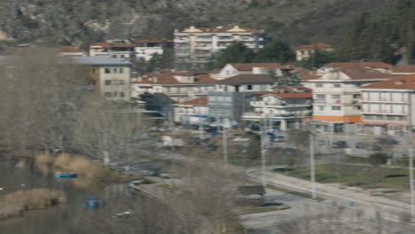 A-pan-left-tripod-movement-of-a-small-town-landscape,-transition-over-the-lake,-clear-water,-sunny-weather,-green-forest-trees-on-the-mountain,-red-rooftops,-European-buildings,-4K-video