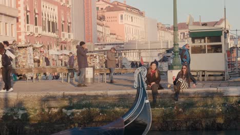 Venetian-gondola-prow-overlooking-a-bustling-canal-promenade