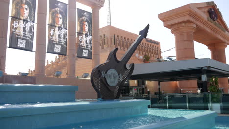 Escultura-Icónica-De-Guitarra-En-El-Hard-Rock-Café-Tenerife,-Enmarcada-Por-Agua-Azul-Y-Pancartas-Que-Dicen-&quot;Historia-De-La-Música&quot;,-Invitando-A-Un-Ambiente-De-Rock-&#39;n&#39;-Roll.