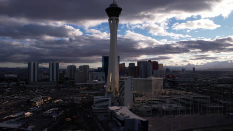 Aerial-View-of-Las-Vegas-Strip-Towers-and-Buildings-Under-Clouds-at-Sunset,-Strat-Tower-in-Front,-Drone-Shot