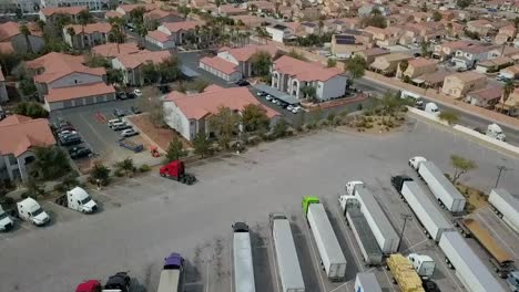 Aerial-flyover-of-Semi-Truck-parking-lot,-apartment-complex-and-residential-neighborhood-with-freeway-at-end