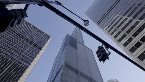 Upward-view-of-Chicago-skyscrapers-against-a-clear-blue-sky,-with-streetlight-and-partial-reflections