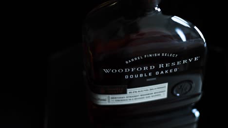Enthüllen-Sie-Eine-Aufnahme-Einer-Flasche-Woodford-Reserve,-Doppelt-Eichenholzgereifter-Kentucky-Straight-Bourbon-Whiskey-90-Proof-Auf-Einem-Dunkelschwarzen-Hintergrund-Mit-Spiegelreflexionen