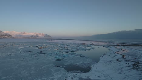 Luftaufnahme,-Zugefrorener-See-Im-Winter,-Faszinierende-Berge-Im-Hintergrund-Bei-Sonnenuntergang