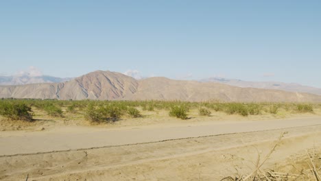 A-Panning-shot-showcasing-an-abandoned-road-in-the-middle-of-of-the-desert-surrounded-by-Mountains-on-a-bright-sunny-day
