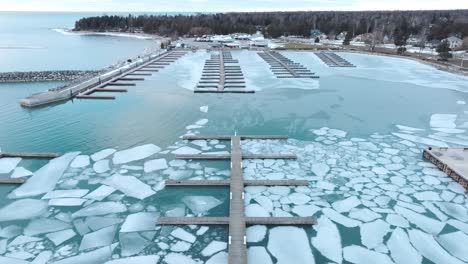 Port-elgin-marina-with-fragmented-ice-sheets-and-empty-docks-in-winter,-aerial-view