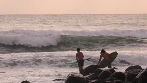 Sunrise-view-of-surfers-diving-into-the-waves-off-the-rocks-at-Burleigh-Heads,-Gold-Coast,-Australia