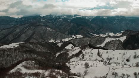 Snow-covered-Cindrel-Mountains-under-a-dramatic-cloudy-sky,-aerial-view