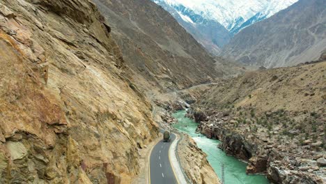 Rear-drone-view-of-truck-driving-through-JSR-Road-by-the-cliff-of-mountains-in-Skardu,-Pakistan