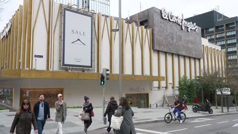 People-wait-at-a-traffic-light-in-front-of-the-Spanish-biggest-department-store-company,-El-Corte-Ingles,-building-in-Spain