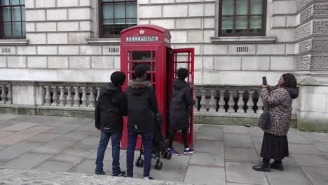 Familia-Africana-Toma-Fotografías-En-Una-Cabina-Telefónica-Roja-A-Lo-Largo-De-Whitehall-Street-En-Londres,-Reino-Unido