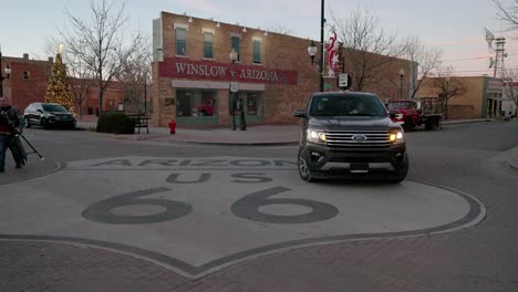 Route-66-Schild-An-Einer-Kreuzung-In-Winslow,-Arizona-Mit-Fahrzeugen-Und-Fußgängern-Mit-Stabilem-Video