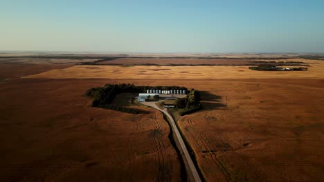 Drone-Aéreo-En-El-Cielo-Azul-Sobre-Una-Pequeña-Granja-Cerrada-En-Medio-De-Una-Gran-Cosecha-Que-Florece-En-Campos-Agrícolas-Canadienses