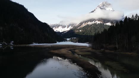 Aerial-dolly-above-low-water-levels-reflect-snow-and-cloud-covered-mountains